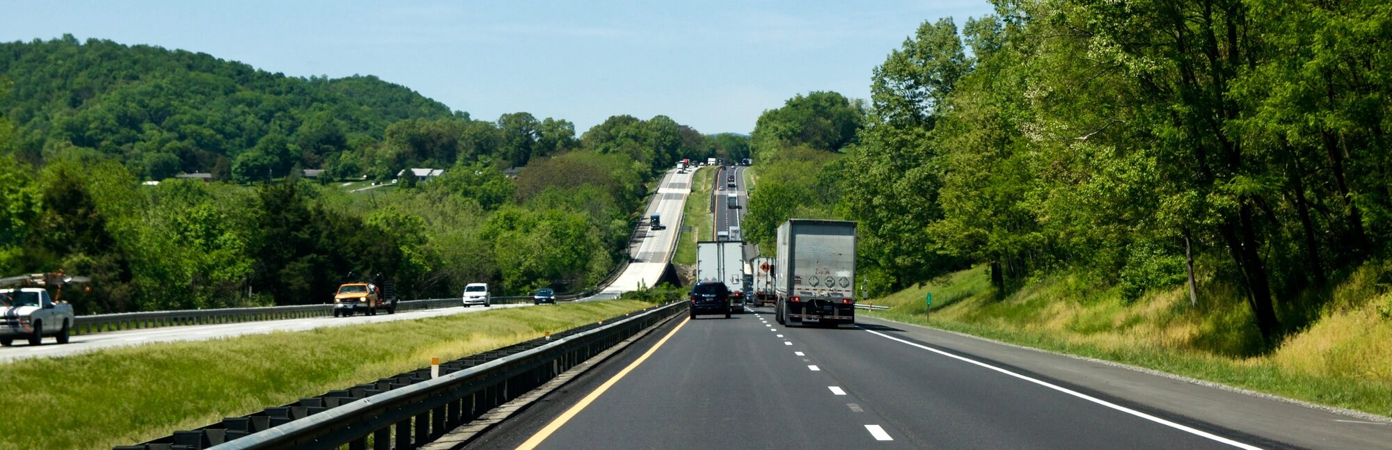 18-wheeler trucks traveling on a country highway surrounded by greenery, illustrating the context of truck accidents and road safety in Alabama.