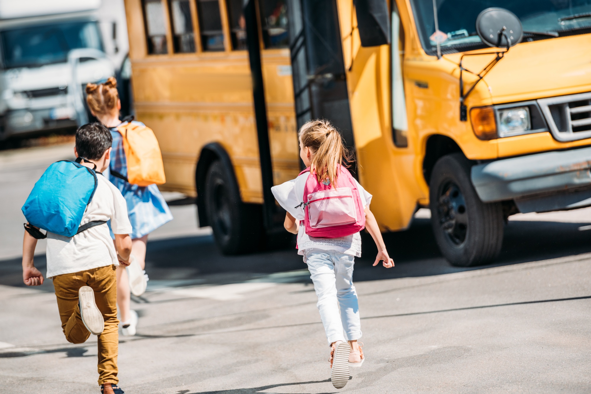 Schoolchildren running towards a yellow school bus, wearing backpacks, illustrating the importance of school bus safety and potential legal issues related to bus accidents.
