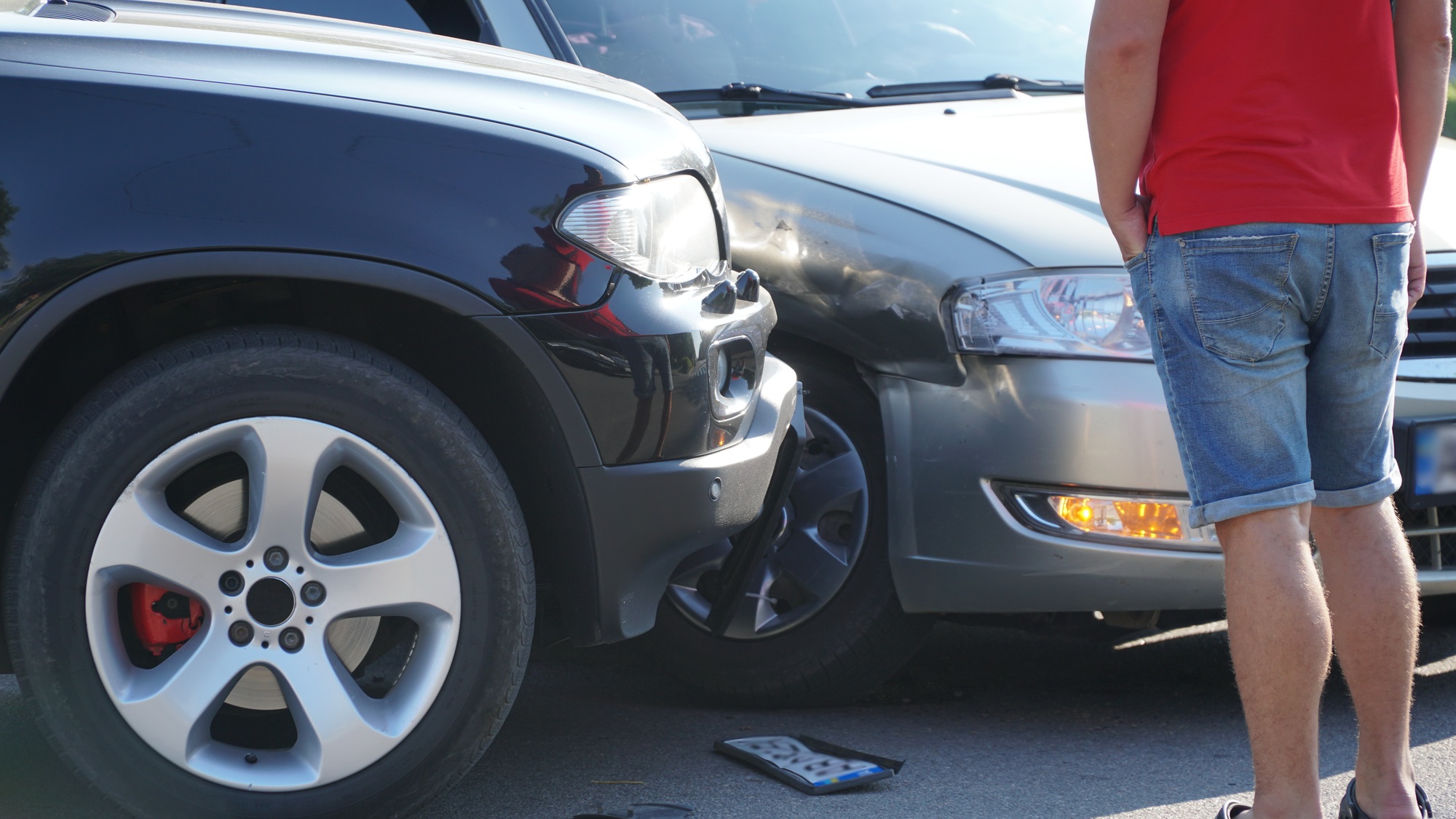 Car accident scene with damaged black and silver vehicles and a person assessing the collision aftermath.